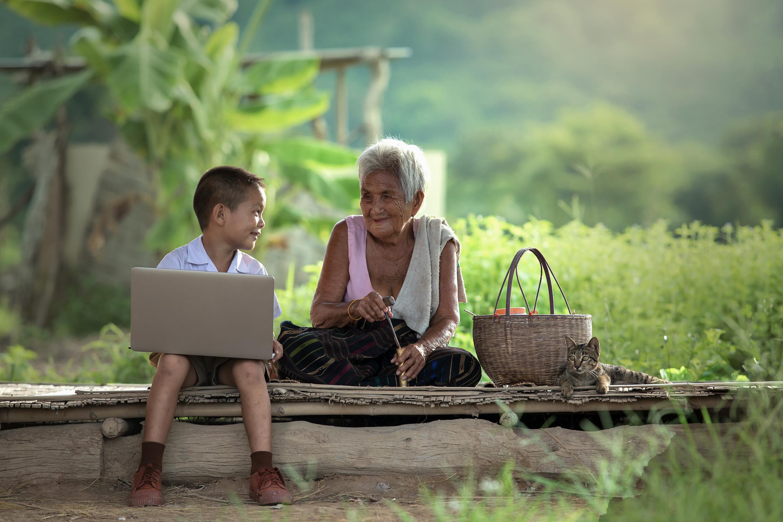 A boy with his grandmother, using a laptop at their cottage