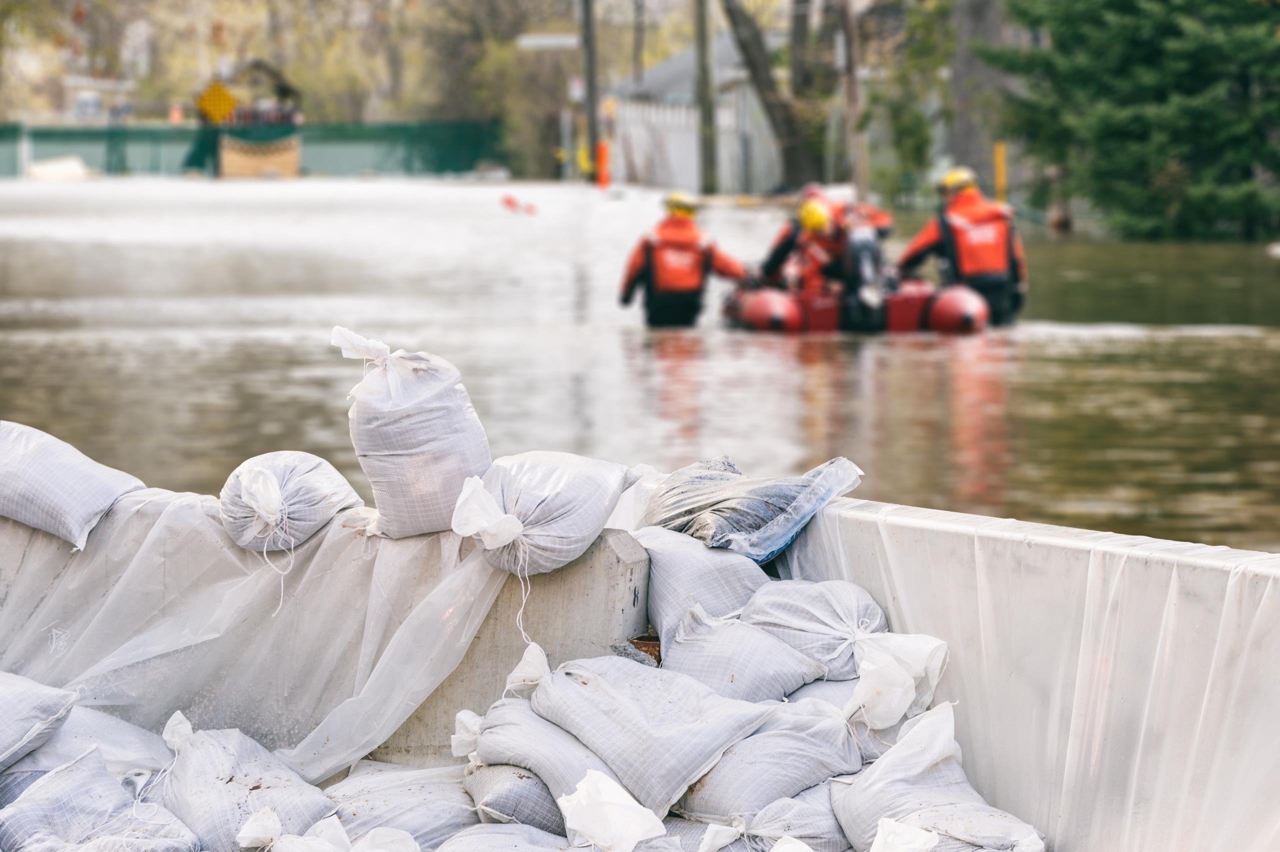A sandbag wall setup to protect against the flood, with a flood rescue team in the background