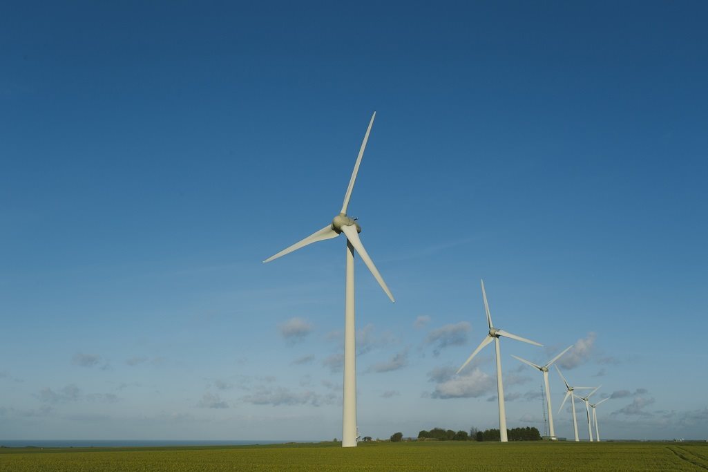 An onshore wind farm in France. The wind farm of five turbines is on green grass and in front of blue sky. 