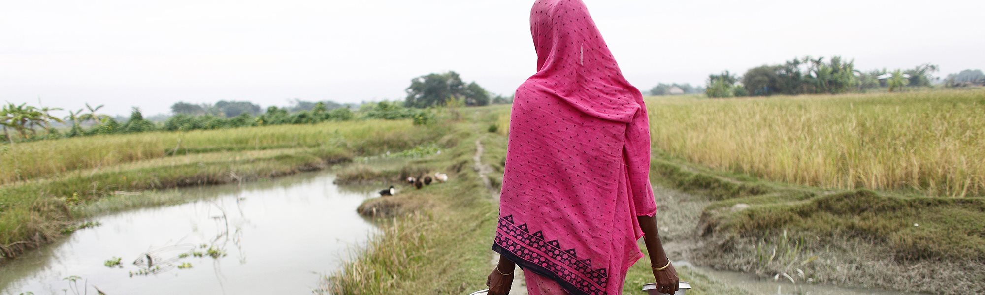 A woman walking by a riverbank holding two pots to collect water