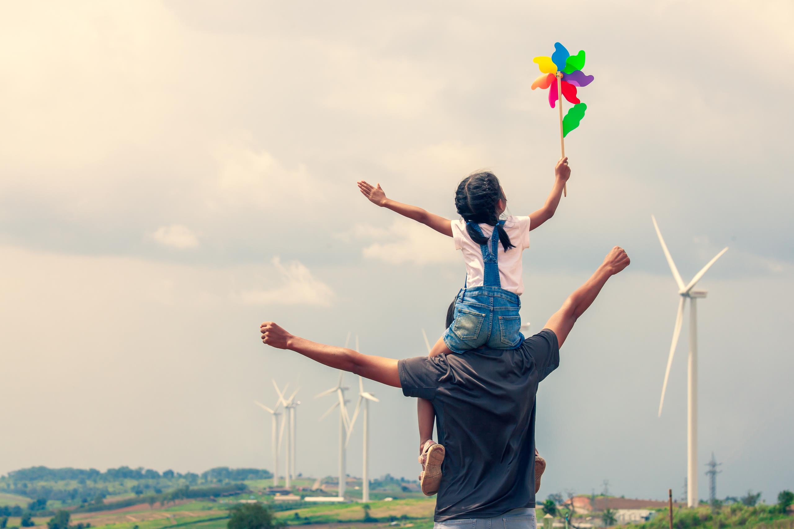A father with his daughter on his shoulders, with a windmill toy in her hand.