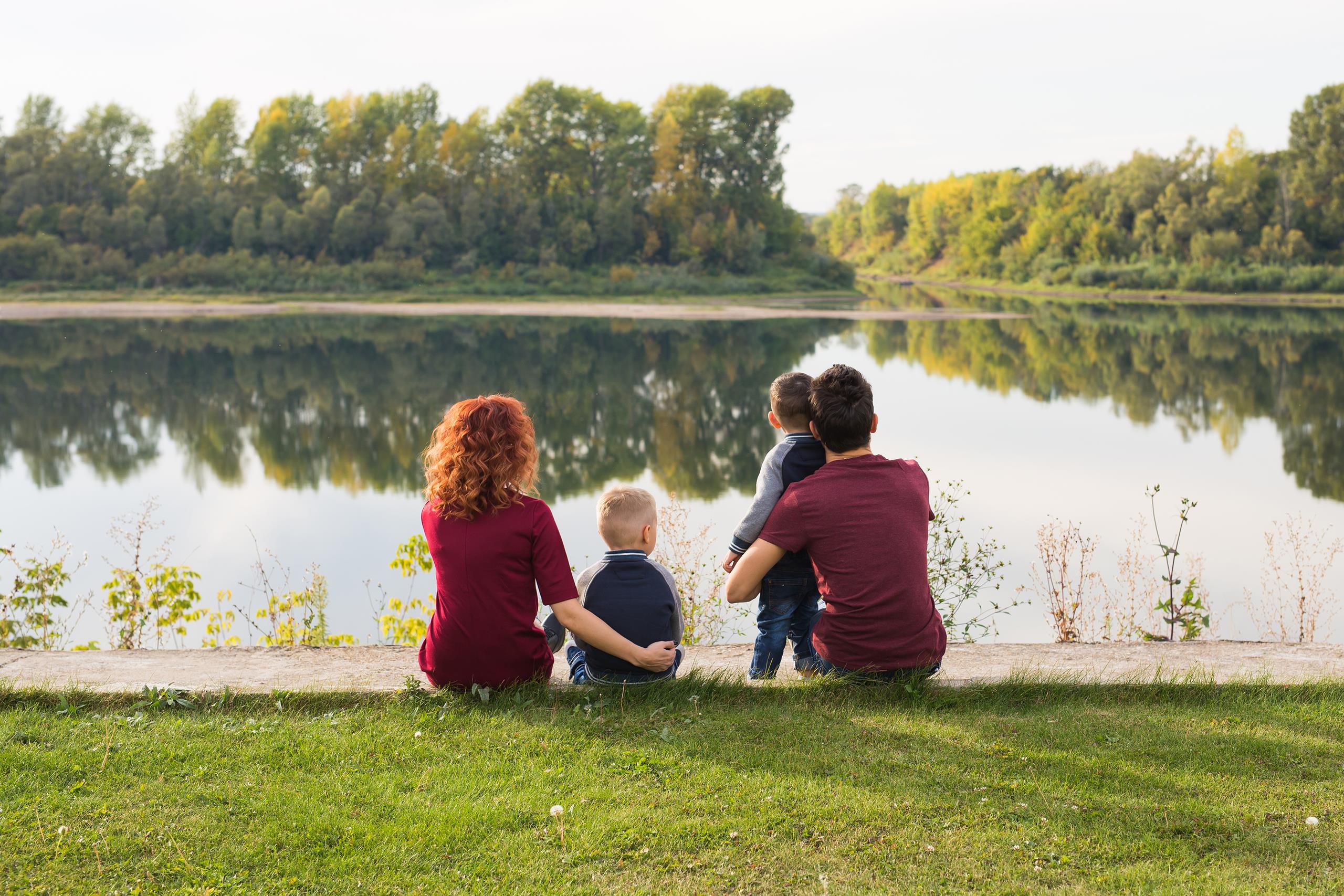 Parents cuddling their children, sat in front of a river with trees on the riverbank in the background