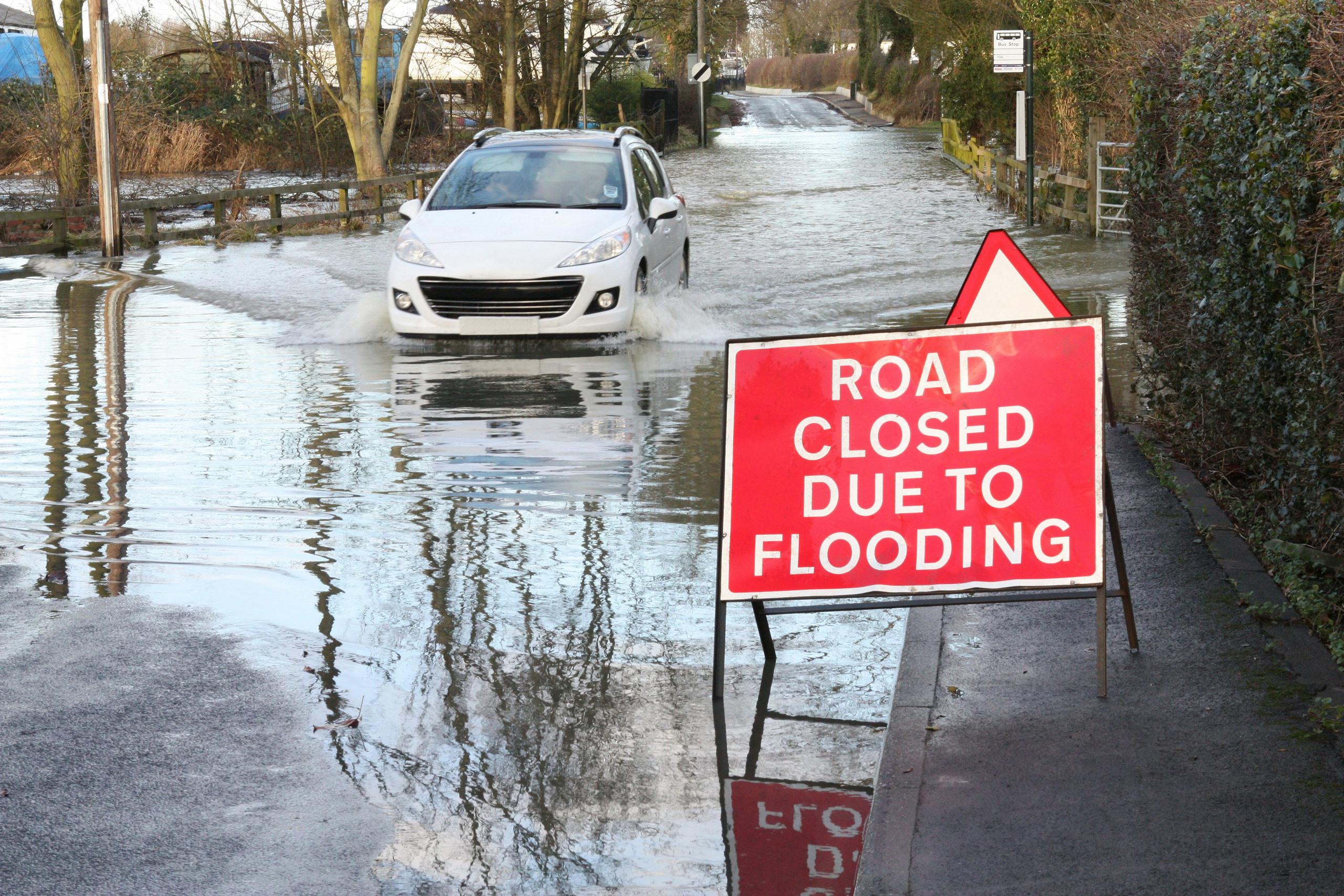 A car driving through a flooded road and ignoring a road closed because of flooding sign.