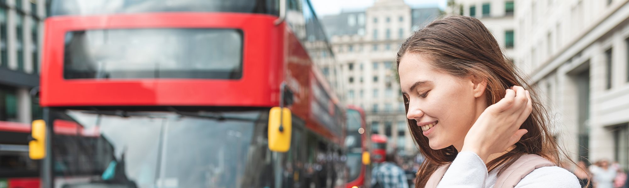 A woman looking at her phone whilst a London bus travels along the road